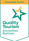 badge featuring a green and gold star, labeled "quality tourism accredited business," on a white background. above, an orange banner reads "sustainable tourism."