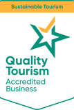 badge featuring a green and gold star, labeled "quality tourism accredited business," on a white background. above, an orange banner reads "sustainable tourism."